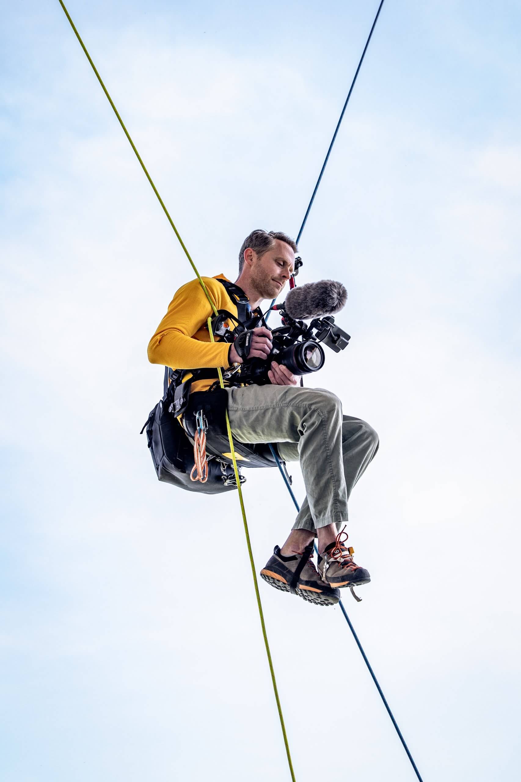 Jan Virt hängt mit Kamera in den Händen an Seilen in der Luft