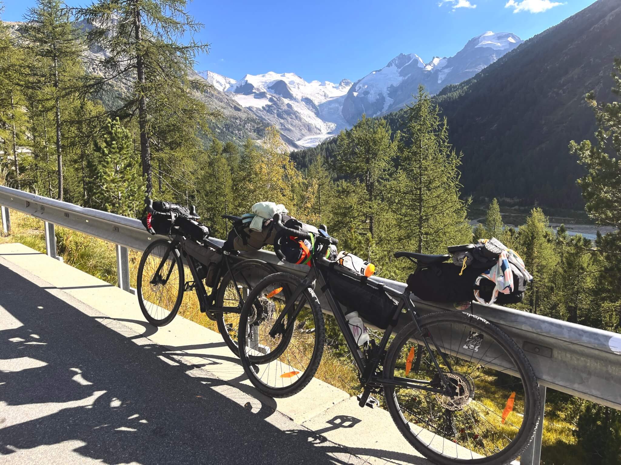 Zwei bepackte Fahrräder an die Leitplanke gelehnt, im Hintergrund schneebedeckte Berge in der Ferne