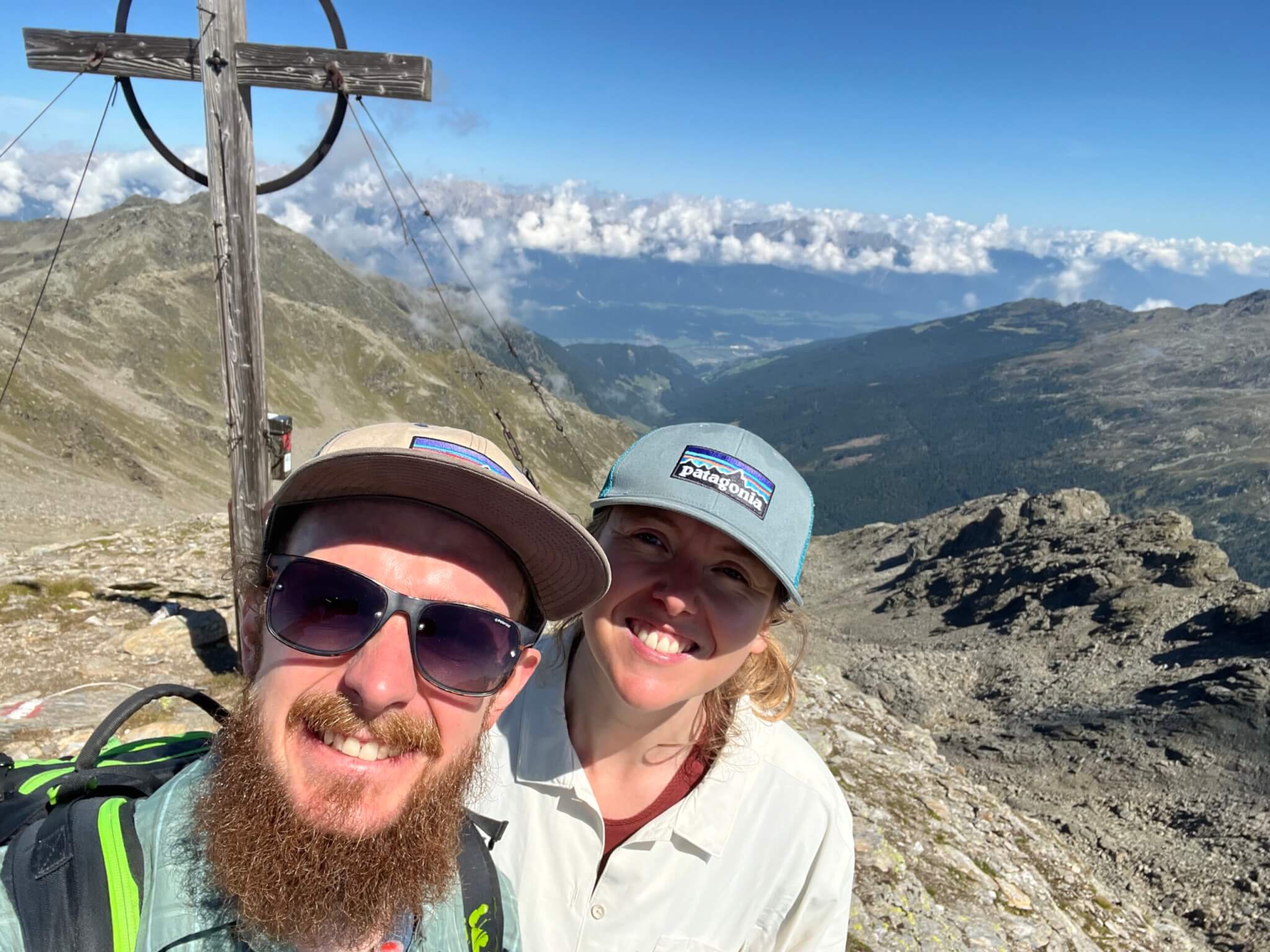 Selfie von Dennis und Elisabeth am Gipfelkreuz, im Hintergrund Bergkulisse