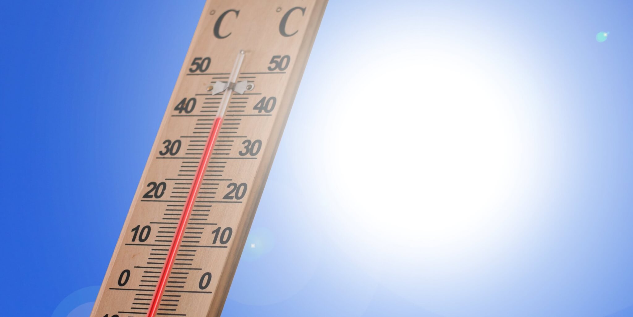 Thermometer zeigt 40 Grad Celsius an, im Hintergrund strahlende Sonne vor blauem Himmel