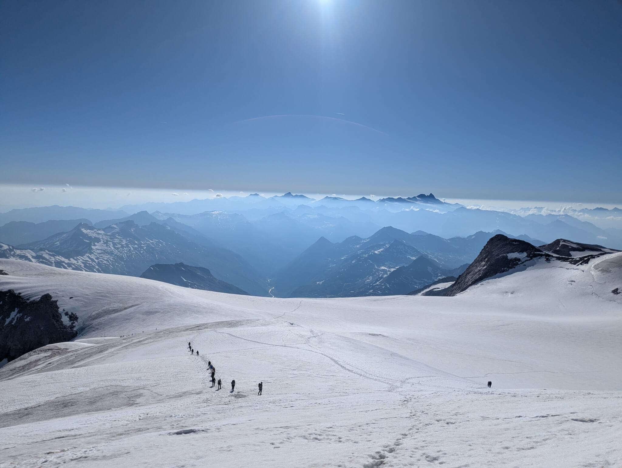 Blick vom Berg aus über den Gletscher Richtung Tal. Auf dem Gletscher ist eine Seilschaft zu sehen.